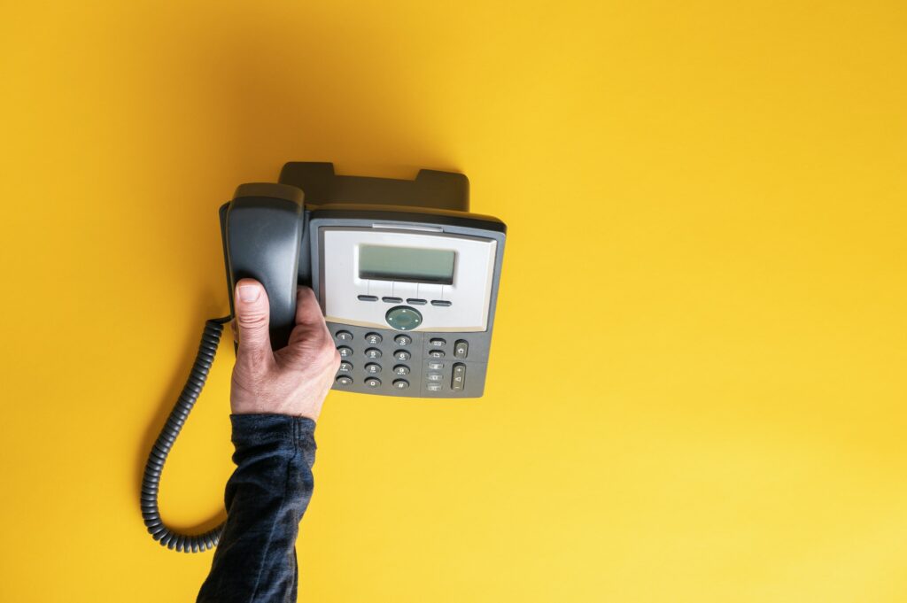 Male hand picking up telephone receiver of a black landline phone